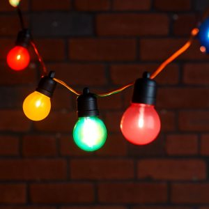 A 10-meter string of coloured festoon lights featuring round, multicoloured LED bulbs (red, green, yellow, blue, and pink) suspended on black fittings against a dark brick wall background. Perfect for decorative and ambient outdoor or indoor lighting.