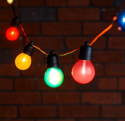 A 10-meter string of coloured festoon lights featuring round, multicoloured LED bulbs (red, green, yellow, blue, and pink) suspended on black fittings against a dark brick wall background. Perfect for decorative and ambient outdoor or indoor lighting.